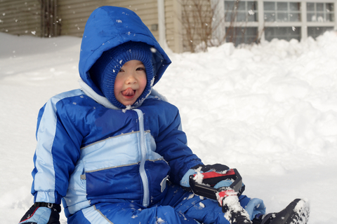 Toddler sitting in the snow licking his face